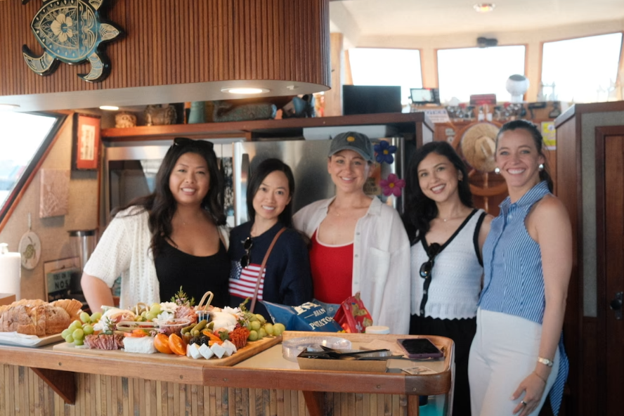 Group of friends posing with charcuterie board inside the Paradise Party Yacht cabin