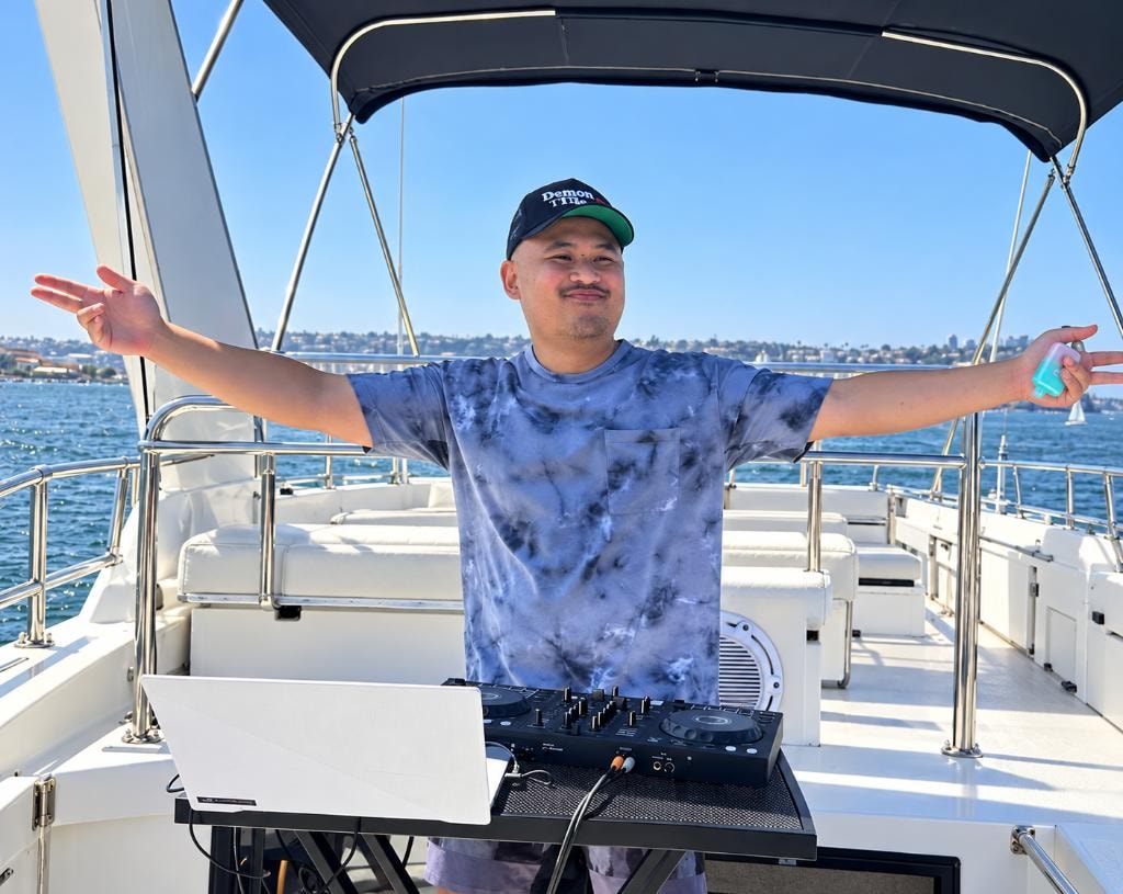 DJ spreading arms wide behind the decks on a private yacht charter on San Diego Bay — DJ party boat rental