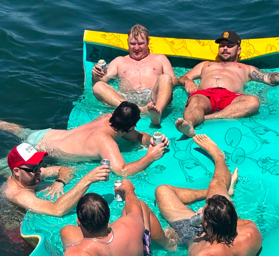 Group of guys relaxing and toasting beers on a floating lily pad during an anchor and swim cruise on San Diego Bay