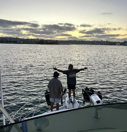 San Diego Bay cruise — guests with arms wide open on private yacht bow at sunset