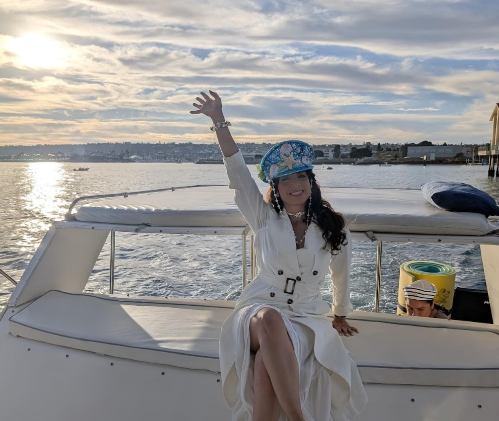 San Diego sunset cruise — woman in white dress waving on private party boat at golden hour on the bay