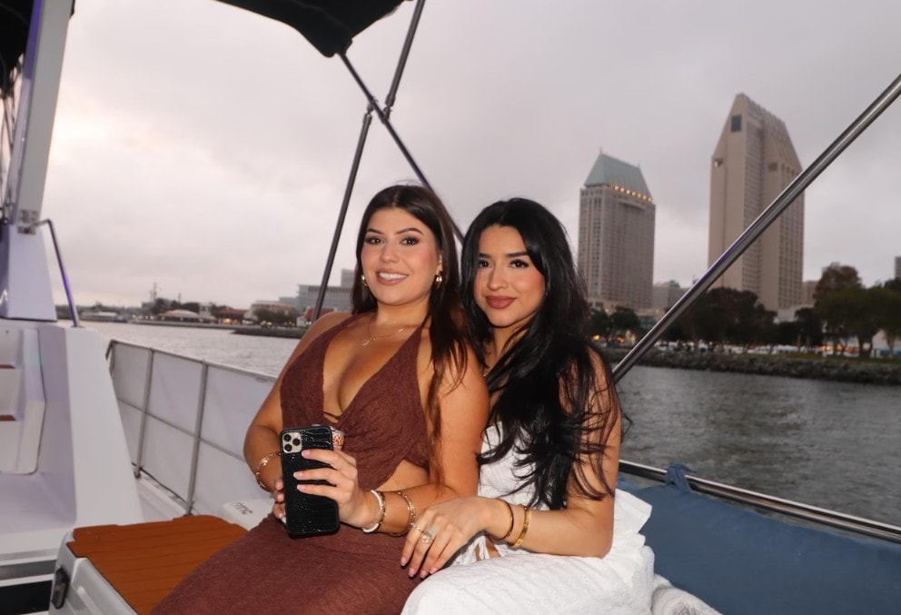 Private yacht charter San Diego — two women on boat at dusk with downtown San Diego skyline backdrop