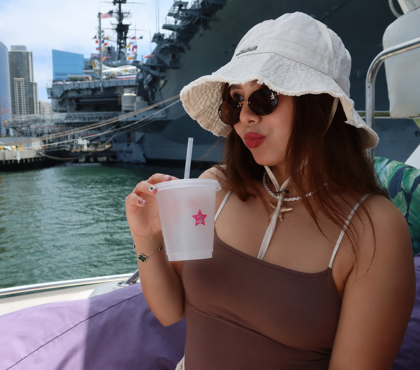 San Diego yacht charter — woman with bucket hat sipping drink on private boat with USS Midway backdrop