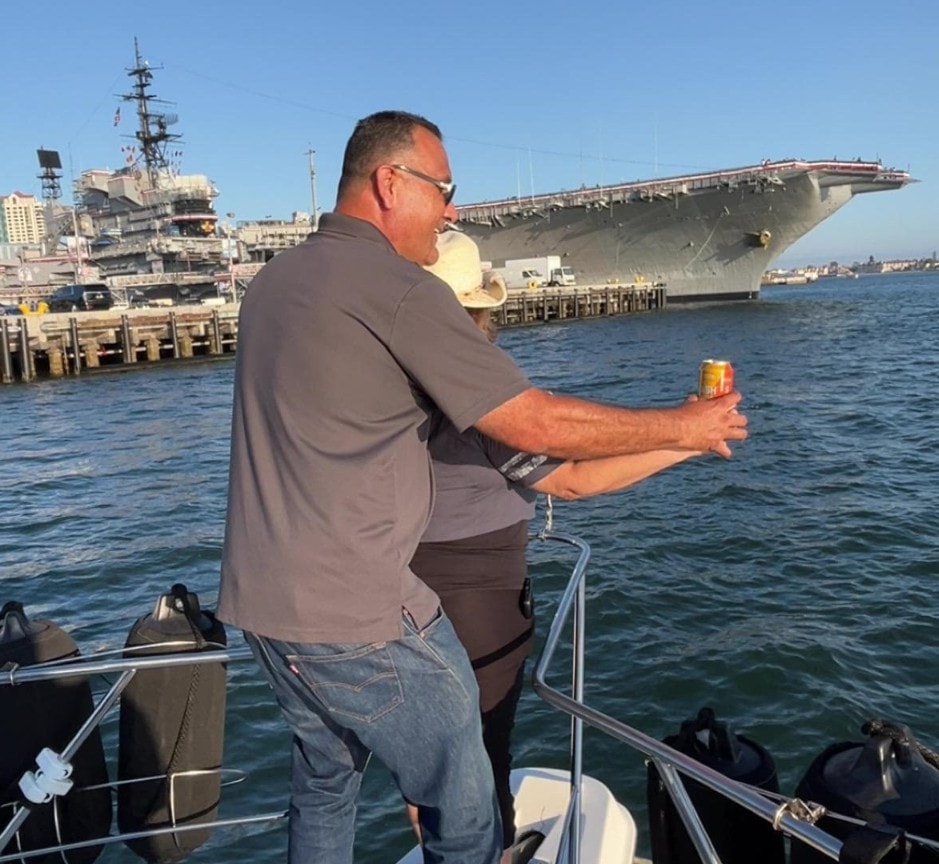 Private party boat San Diego — man with beer on yacht near USS Midway aircraft carrier on San Diego Bay